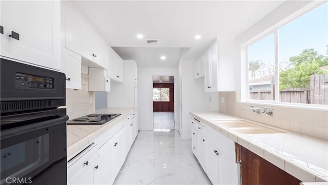 kitchen with white cabinets, tile counters, sink, stainless steel gas cooktop, and oven