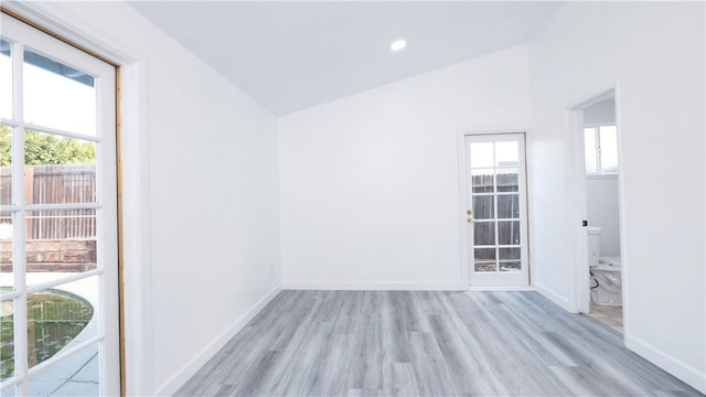 unfurnished room featuring a healthy amount of sunlight, vaulted ceiling, and light hardwood / wood-style floors