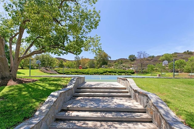 surrounding community with a mountain view, basketball hoop, and a yard