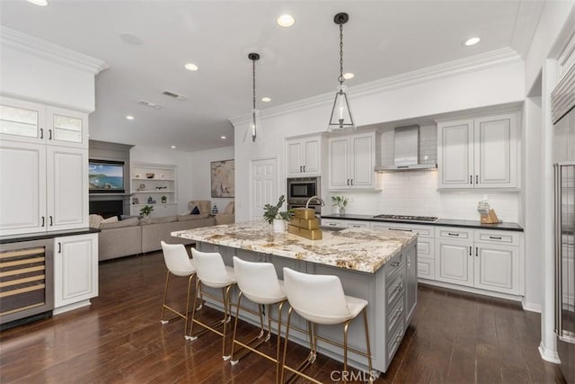 kitchen featuring a kitchen bar, light stone countertops, decorative light fixtures, a center island with sink, and wall chimney exhaust hood