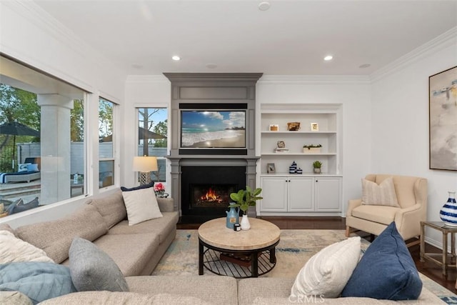 living room featuring a large fireplace, wood-type flooring, crown molding, and built in features