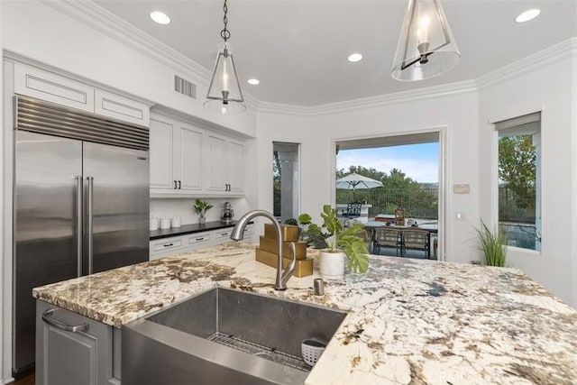 kitchen featuring crown molding, pendant lighting, sink, built in refrigerator, and dark stone countertops