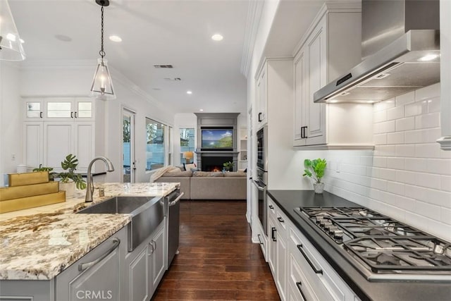 kitchen featuring white cabinets, appliances with stainless steel finishes, wall chimney range hood, sink, and ornamental molding