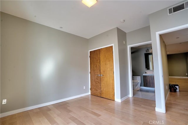 unfurnished bedroom with ensuite bathroom, a closet, and light hardwood / wood-style flooring