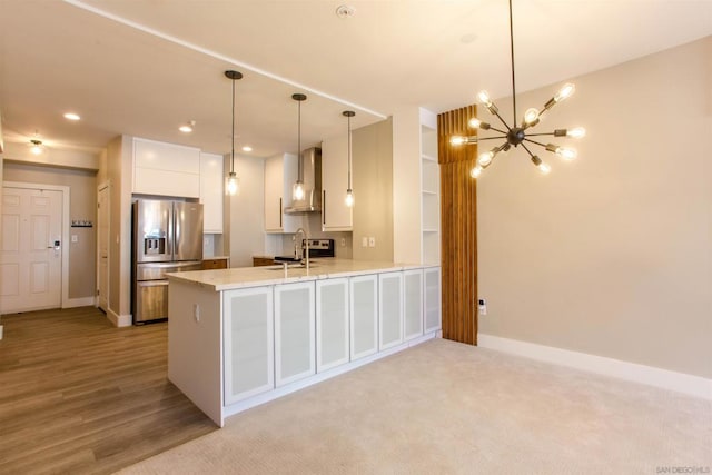 kitchen featuring stainless steel refrigerator with ice dispenser, kitchen peninsula, hanging light fixtures, white cabinets, and wall chimney exhaust hood