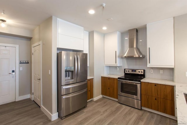 kitchen featuring white cabinetry, wall chimney range hood, stainless steel appliances, decorative backsplash, and light wood-type flooring