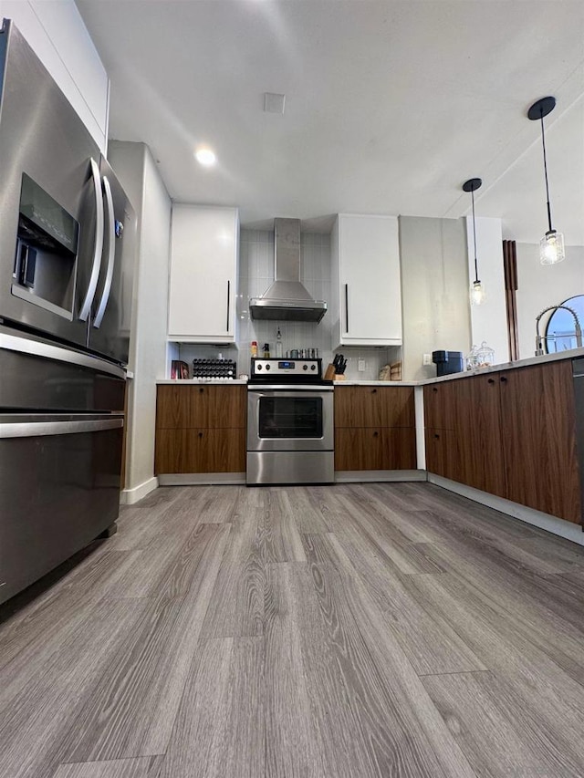 kitchen with appliances with stainless steel finishes, wall chimney range hood, white cabinetry, and pendant lighting