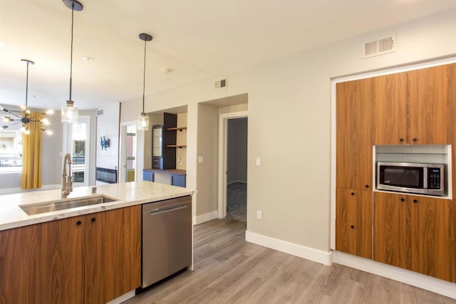 kitchen with light hardwood / wood-style floors, pendant lighting, sink, stainless steel appliances, and a chandelier