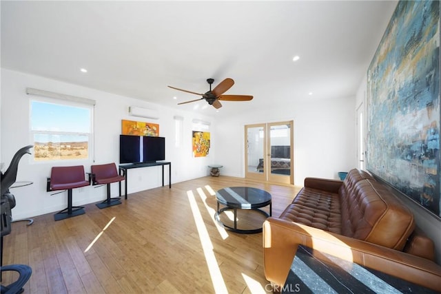 living room with ceiling fan, plenty of natural light, light hardwood / wood-style floors, and a wall mounted air conditioner