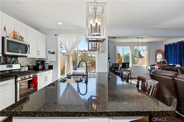 kitchen featuring a spacious island, appliances with stainless steel finishes, dark stone countertops, sink, and hanging light fixtures