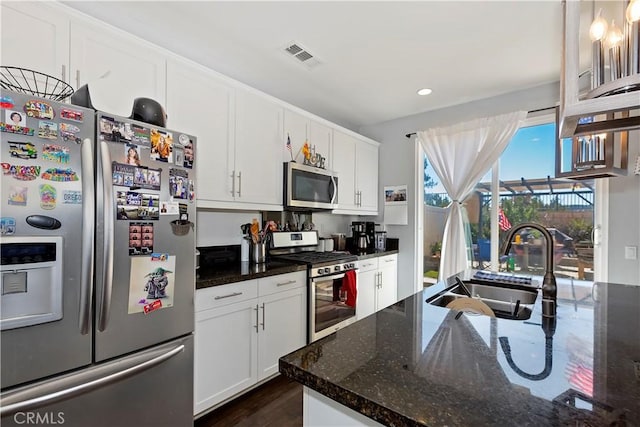 kitchen featuring white cabinets, dark wood-type flooring, stainless steel appliances, dark stone counters, and sink