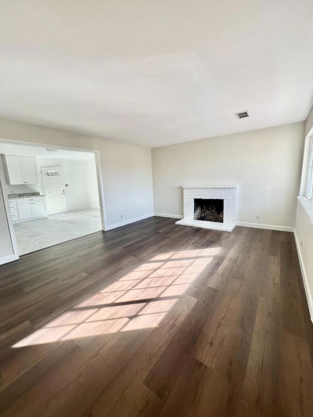 unfurnished living room featuring a brick fireplace and dark hardwood / wood-style flooring