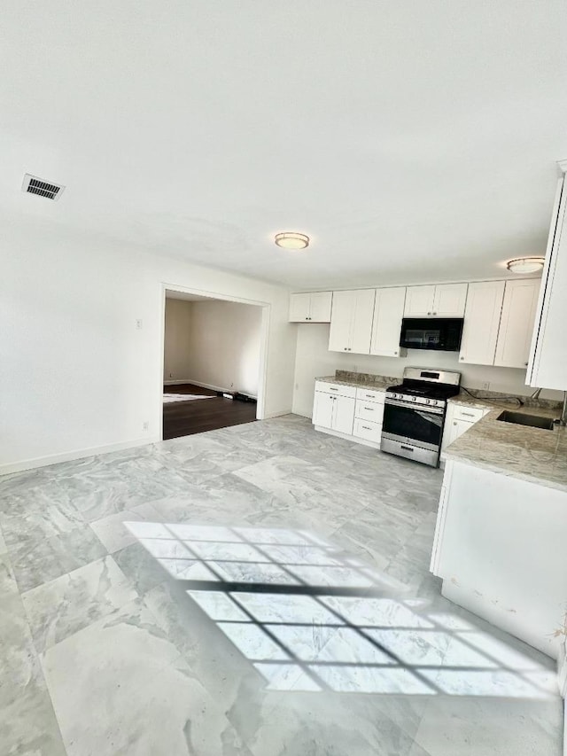 kitchen featuring stainless steel stove, white cabinetry, light stone counters, and sink