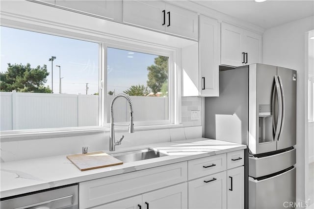 kitchen featuring light stone countertops, white cabinets, stainless steel appliances, sink, and backsplash