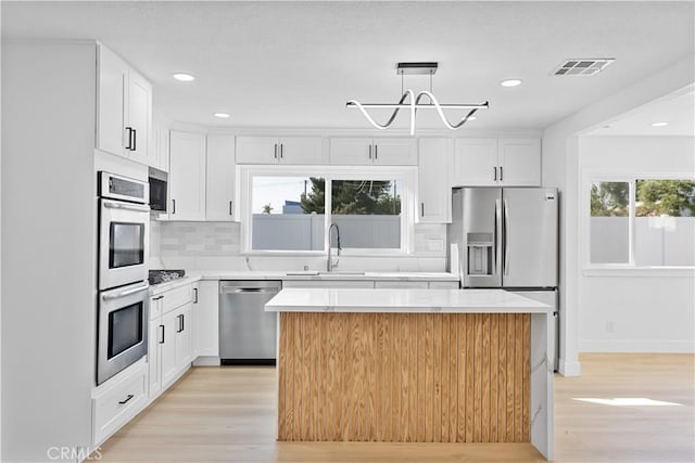 kitchen featuring stainless steel appliances, white cabinetry, tasteful backsplash, and a center island