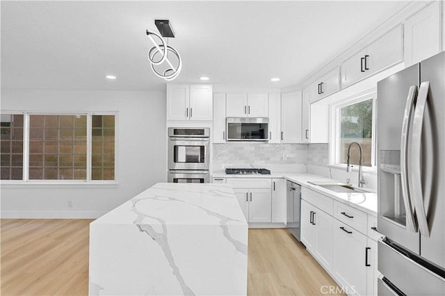 kitchen featuring sink, hanging light fixtures, stainless steel appliances, white cabinets, and light stone counters