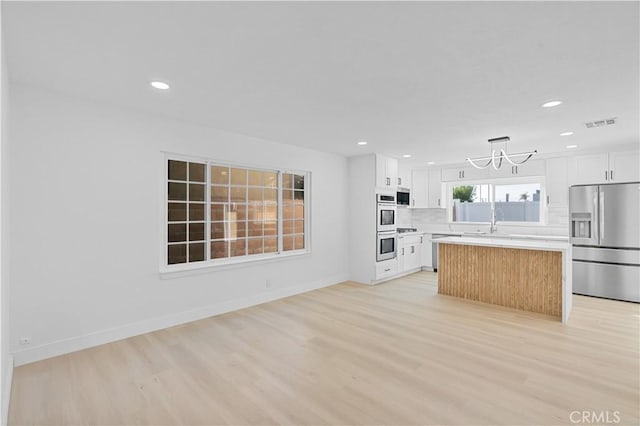 kitchen with white cabinets, appliances with stainless steel finishes, a center island, light hardwood / wood-style floors, and hanging light fixtures