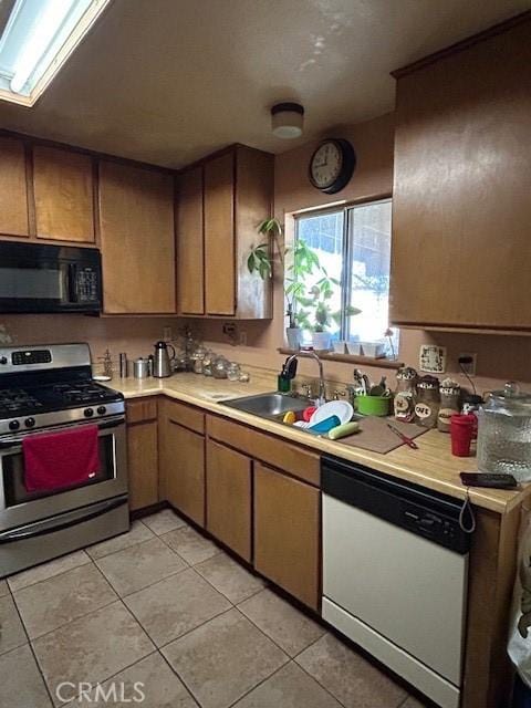 kitchen with light tile patterned floors, white dishwasher, stainless steel gas stove, and sink