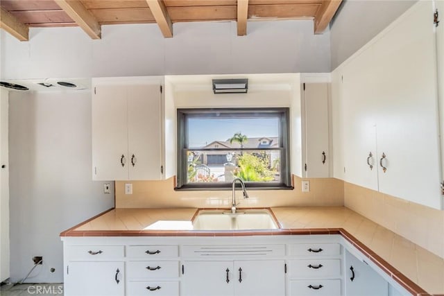 kitchen with tile counters, wood ceiling, white cabinetry, beamed ceiling, and sink