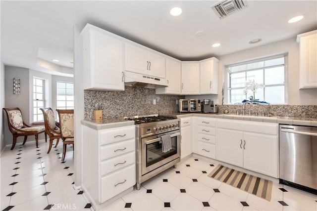 kitchen with appliances with stainless steel finishes, white cabinetry, tasteful backsplash, and tile counters