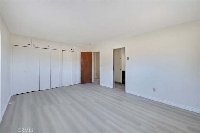 unfurnished bedroom featuring light wood-type flooring and multiple closets