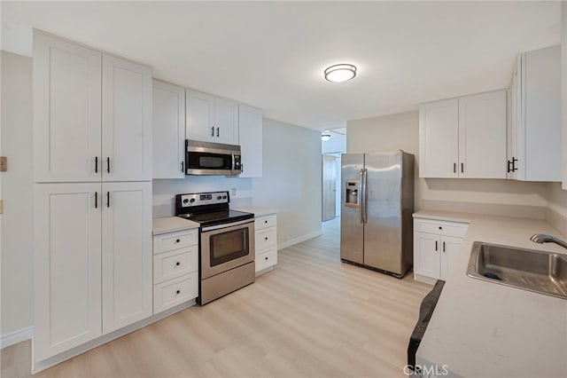 kitchen with stainless steel appliances, light hardwood / wood-style floors, white cabinets, and sink