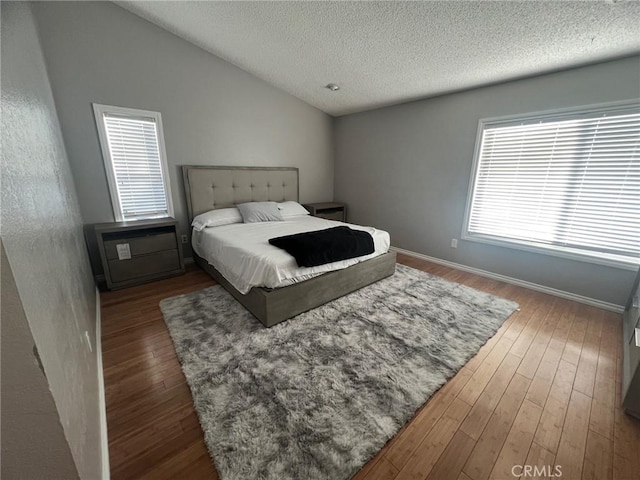 bedroom featuring a textured ceiling, dark hardwood / wood-style flooring, vaulted ceiling, and multiple windows