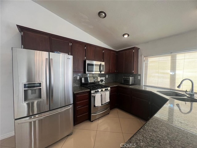 kitchen featuring vaulted ceiling, dark stone countertops, sink, light tile patterned flooring, and stainless steel appliances