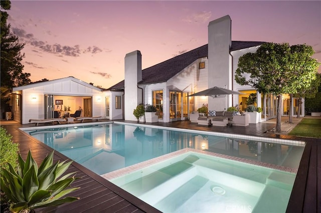 pool at dusk featuring an in ground hot tub, an outdoor hangout area, and an outdoor structure