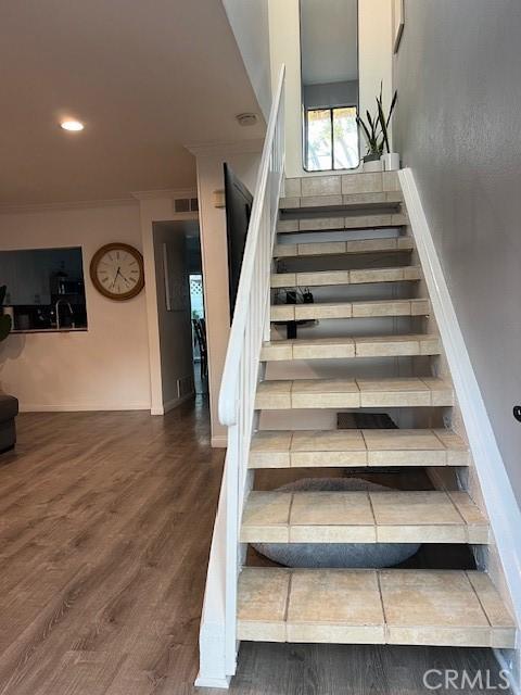 stairs featuring wood-type flooring and crown molding