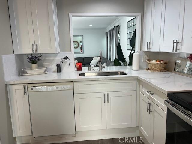 kitchen featuring decorative backsplash, sink, white dishwasher, white cabinetry, and light stone counters