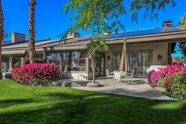 rear view of property featuring a lawn, solar panels, and a patio