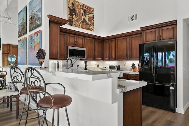 kitchen featuring a high ceiling, black refrigerator, wood-type flooring, kitchen peninsula, and a breakfast bar area