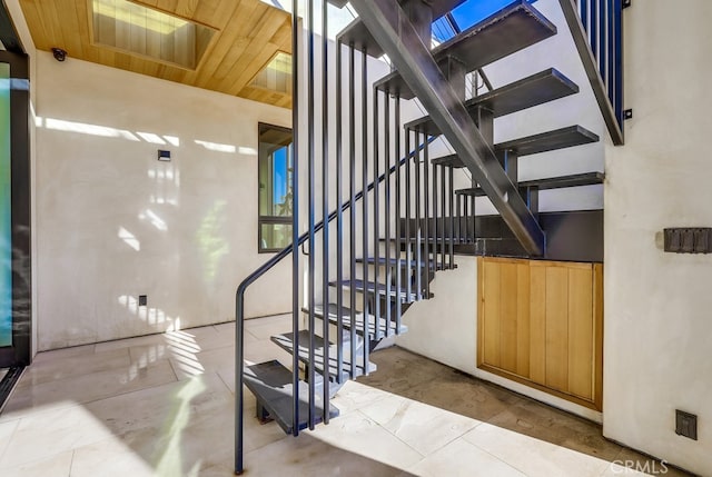 staircase with a skylight, a towering ceiling, and wooden ceiling