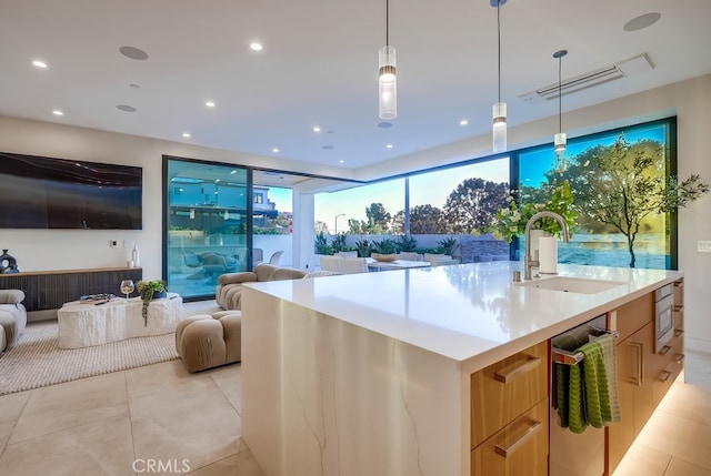 kitchen featuring sink, hanging light fixtures, a kitchen island with sink, light tile patterned floors, and light brown cabinetry