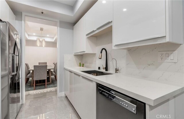 kitchen featuring dishwasher, sink, white cabinets, stainless steel fridge, and a raised ceiling