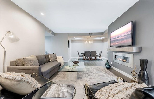 living room featuring a glass covered fireplace, visible vents, baseboards, and wood finished floors