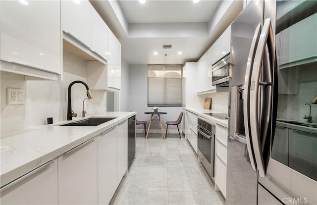 kitchen with sink, light stone counters, tasteful backsplash, black appliances, and white cabinets