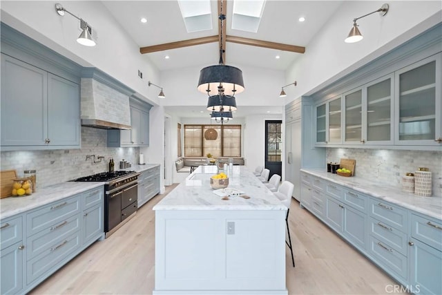 kitchen featuring double oven range, a kitchen island, light wood-style floors, wall chimney exhaust hood, and glass insert cabinets