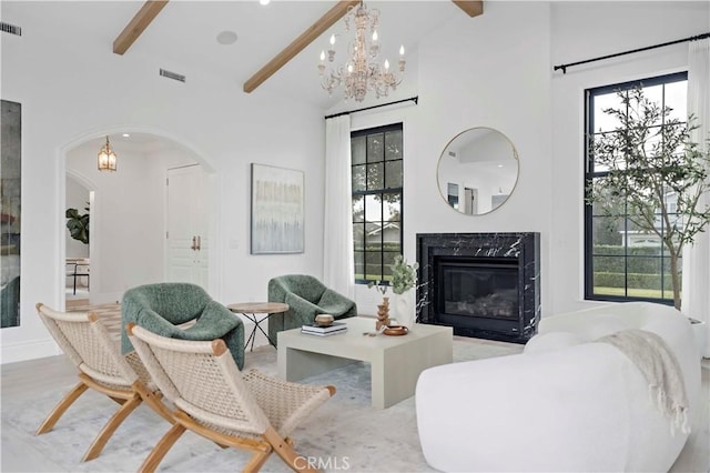 living area featuring beam ceiling, plenty of natural light, a chandelier, and a high end fireplace