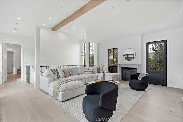 living area with baseboards, lofted ceiling with beams, recessed lighting, light wood-style floors, and a glass covered fireplace