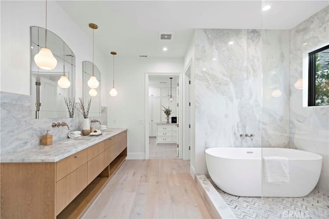 bathroom with hardwood / wood-style flooring, vanity, a bath, and tile walls