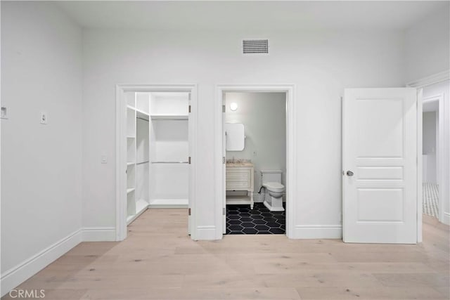 unfurnished bedroom with a closet, a walk in closet, ensuite bath, and light hardwood / wood-style flooring