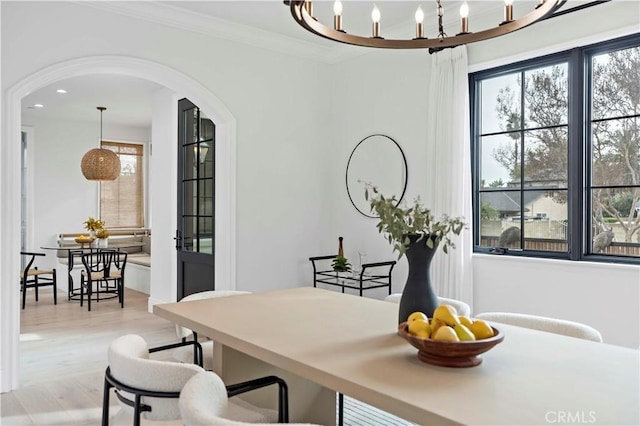 dining space with light wood-type flooring, a notable chandelier, recessed lighting, arched walkways, and crown molding