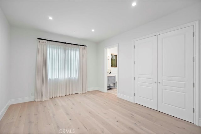 unfurnished bedroom with a closet, connected bathroom, and light hardwood / wood-style flooring