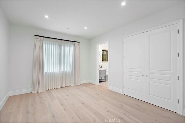 unfurnished bedroom featuring baseboards, recessed lighting, ensuite bathroom, light wood-style floors, and a closet