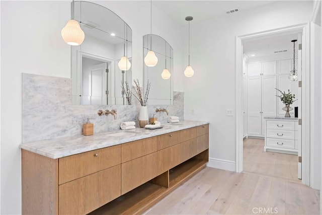 full bath with tasteful backsplash, visible vents, double vanity, wood finished floors, and a sink