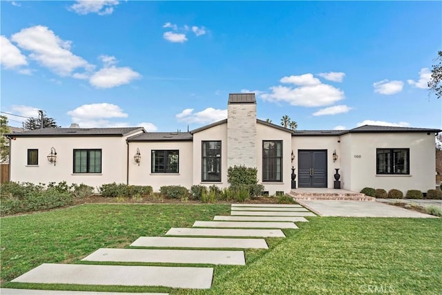 view of front of house with stucco siding, a chimney, and a front yard