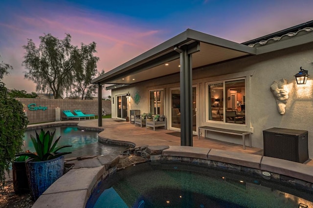 pool at dusk with an in ground hot tub and a patio