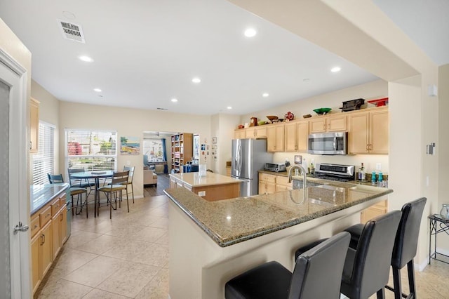 kitchen with stainless steel appliances, a large island with sink, light brown cabinets, and a breakfast bar